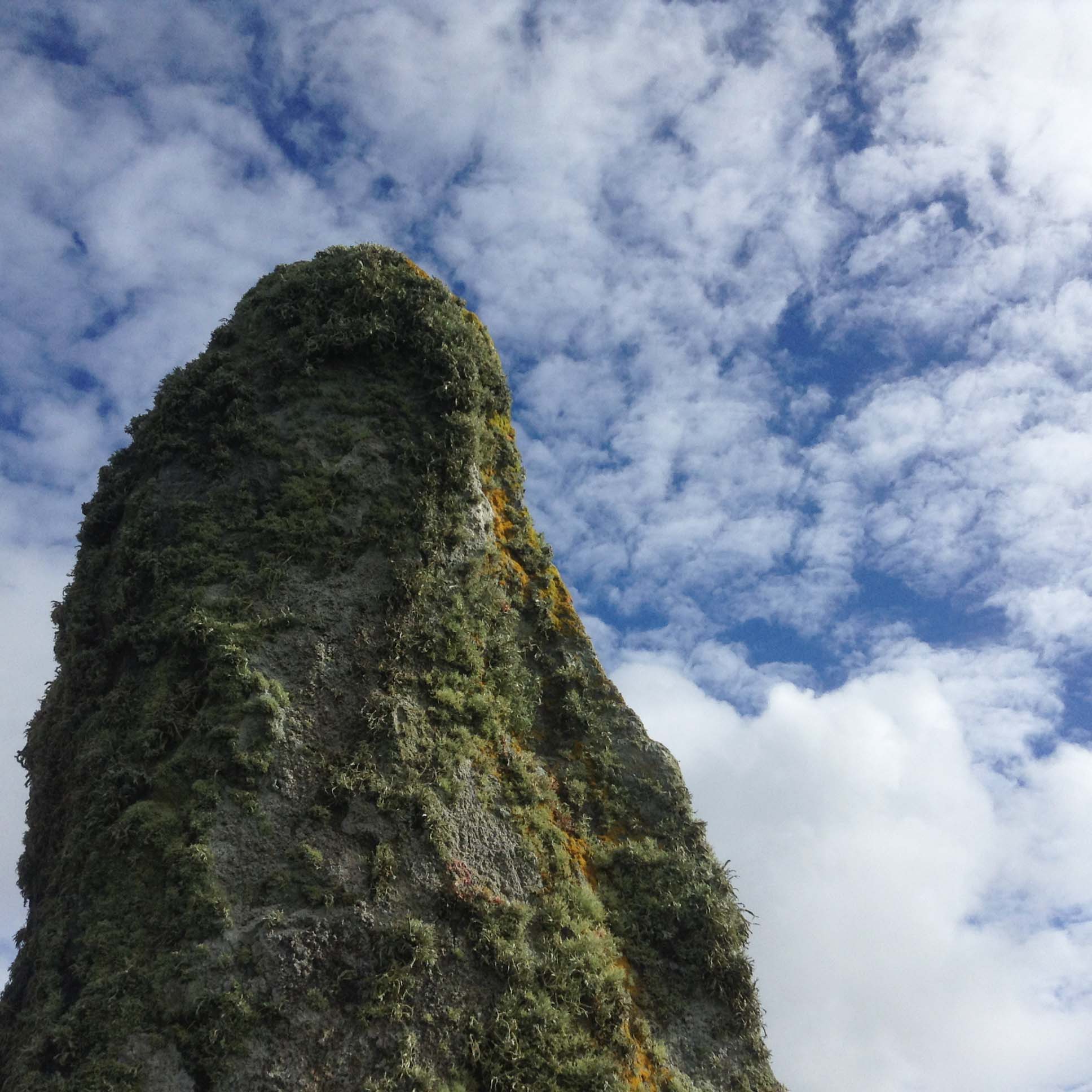 Moss-covered standing stone silhouetted against clouds and blue sky