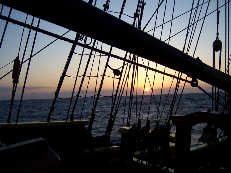 The sun setting through the rigging of a tall ship